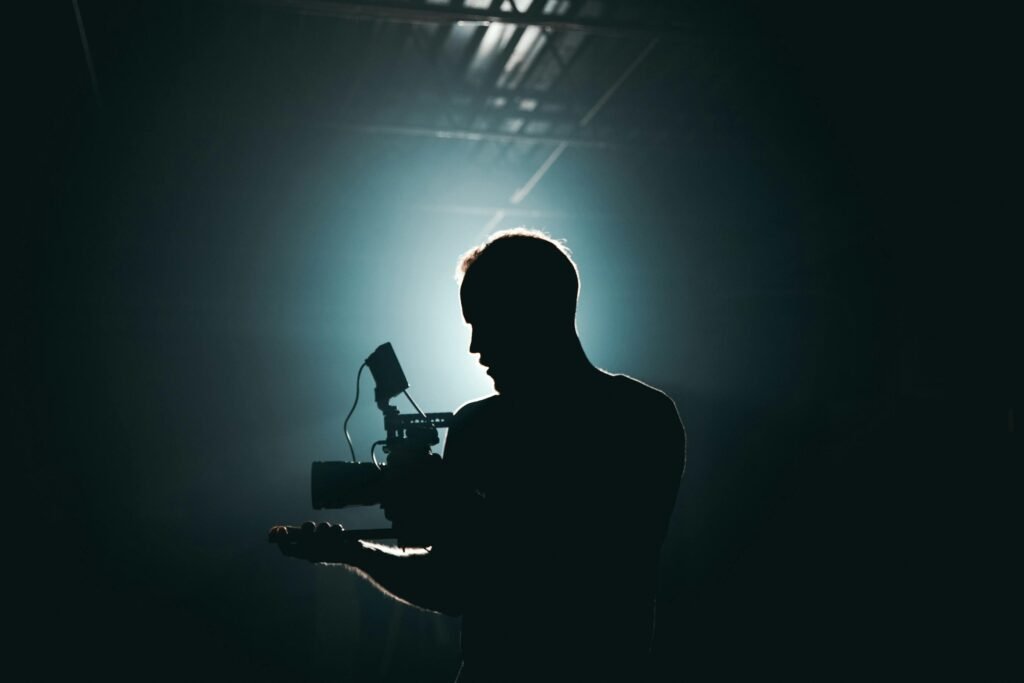 Silhouette of a cinematographer with camera gear in a dramatic, low light setting.